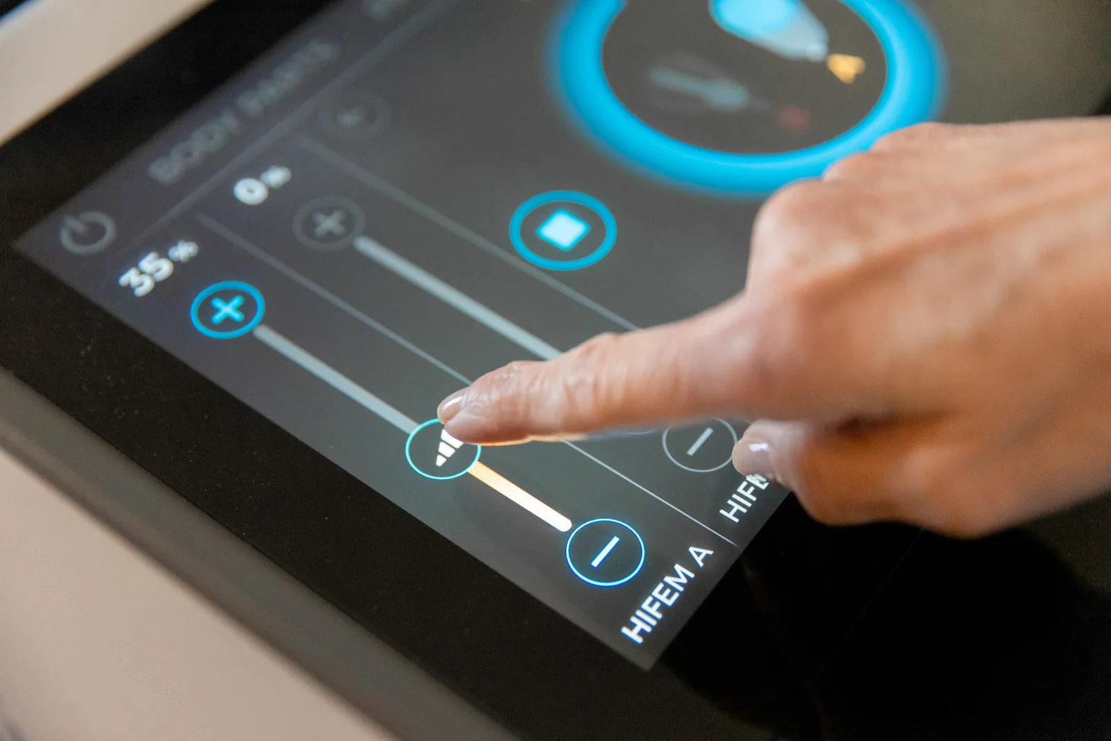 Fingertip adjusting an intensity slider on a touchscreen control panel, with a percentage readout and a label reading HIFEM A.