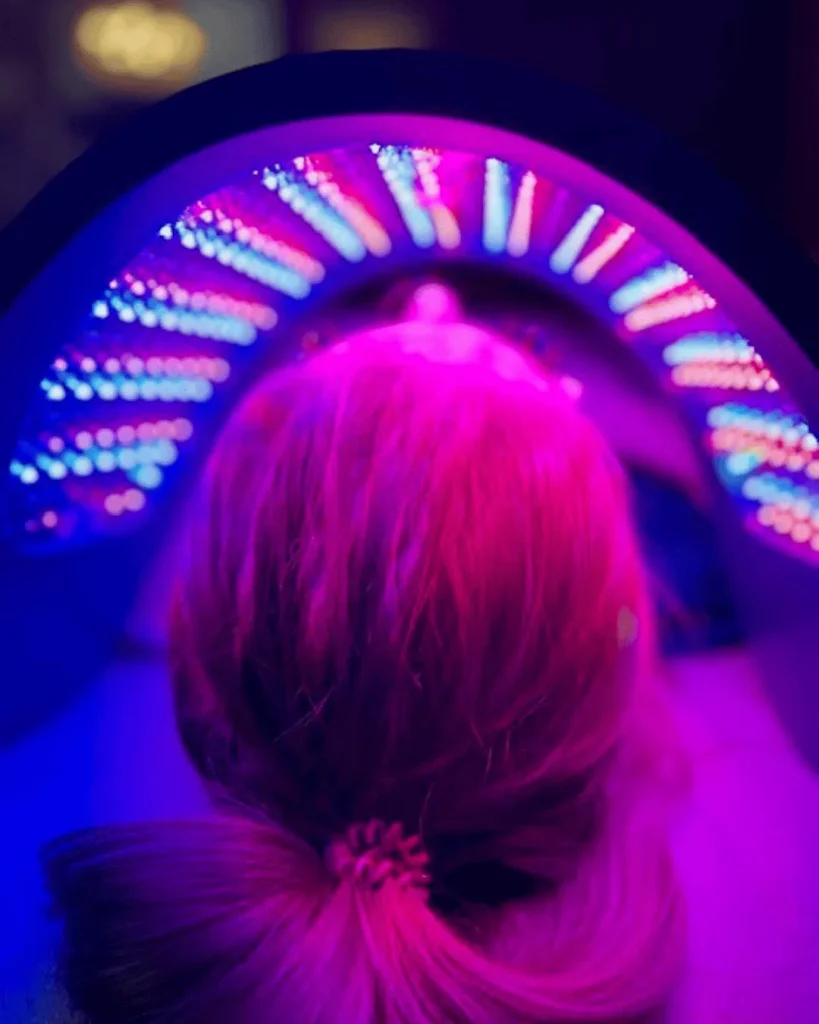 Close-up from behind of a person's head under an arched LED light panel glowing pink, red, and blue.