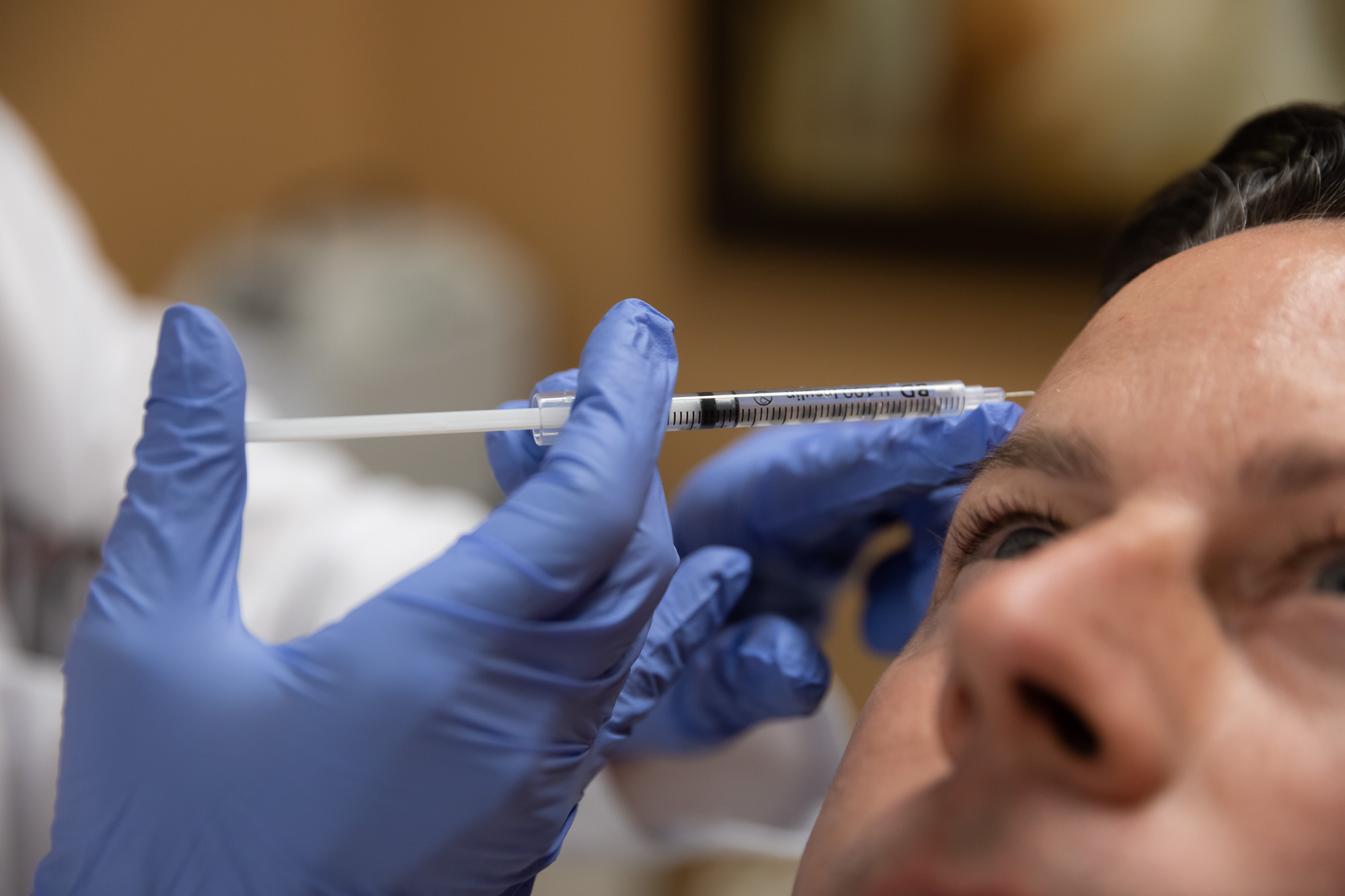 Gloved hands hold a syringe against a man's forehead near his eyebrow during a wrinkle relaxer treatment at Catara Med Spa in Algonquin, IL.