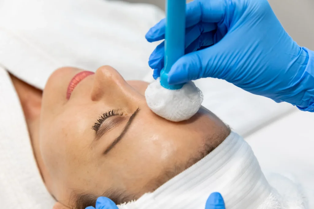 Gloved hand pressing a cotton tipped applicator with a blue handle against a reclining person's cheek near the nose.