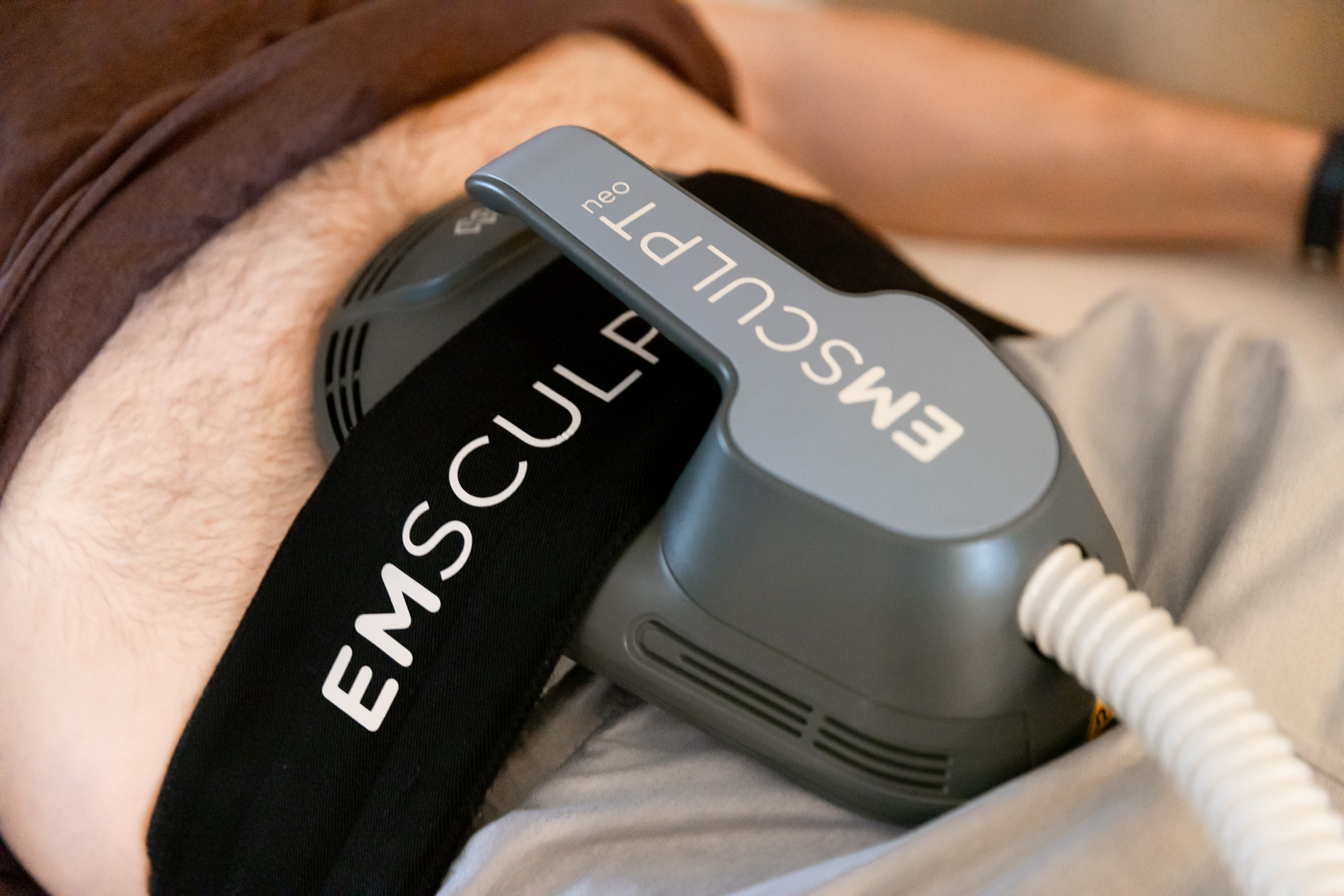 Close-up of an Emsculpt Neo device applicator secured with its branded strap during a muscle-toning treatment at Catara Med Spa in Algonquin, IL.