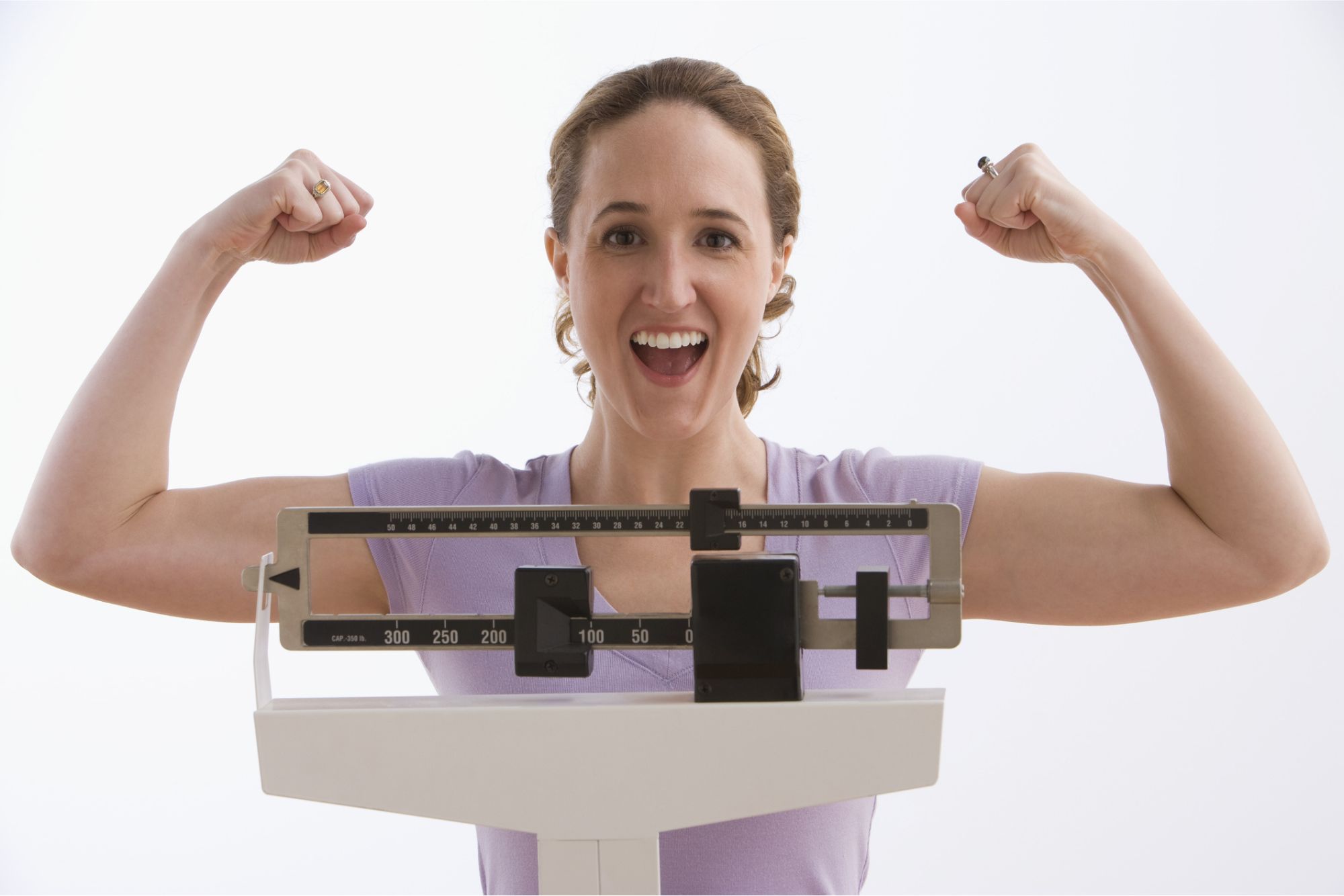 Happy woman flexing muscles after weight loss success on scale at Catara Med Spa Algonquin IL, semaglutide and body transformation program.