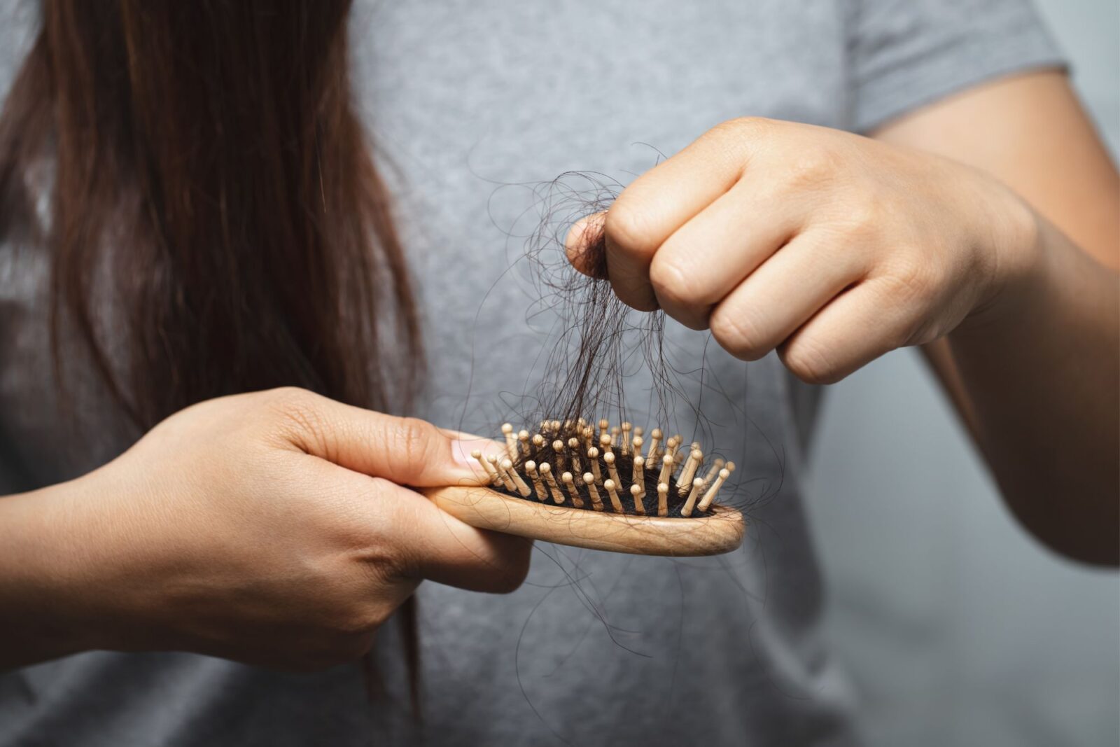 Close-up of a woman's hands holding a hairbrush tangled with loose hair, more strands held in her other fist above it.