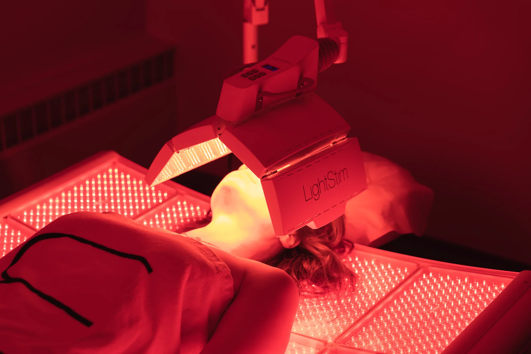 Client lying beneath a LightStim red LED therapy panel at Catara Med Spa in Algonquin, IL, their face lit by the red light array.
