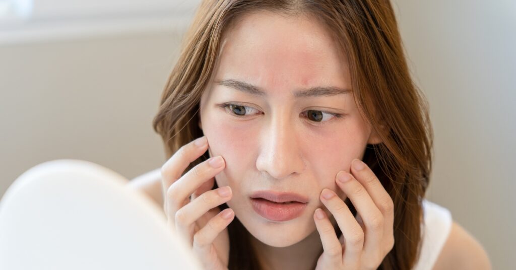 Woman examining her face in the mirror after dermaplaning treatment at Catara Med Spa in Algonquin, IL. Smooth skin with no thicker hair regrowth.