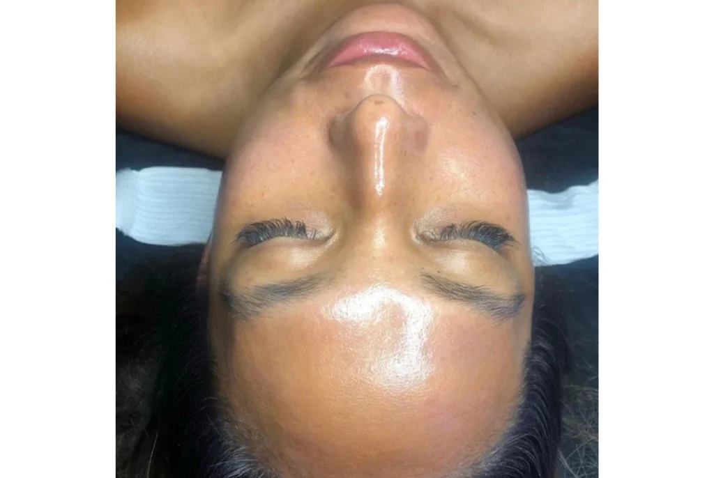 Upside-down close-up of a woman's face, eyes closed, glossy skin with a bright highlight along the nose and forehead.